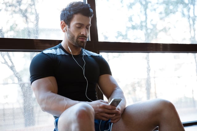 Athletic man wearing black t-shirt listening to music sitting on windowcill.jpeg