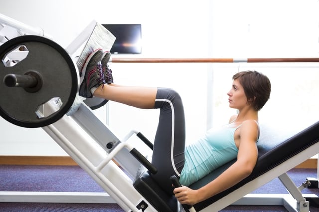 Fit brunette using weights machine for legs at the gym.jpeg